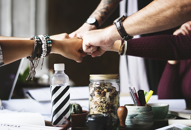 Hands of colleagues fist-bumping over a table with stationery.