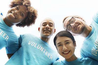 Four volunteers smiling, wearing blue shirts with the word 'VOLUNTEER' visible.