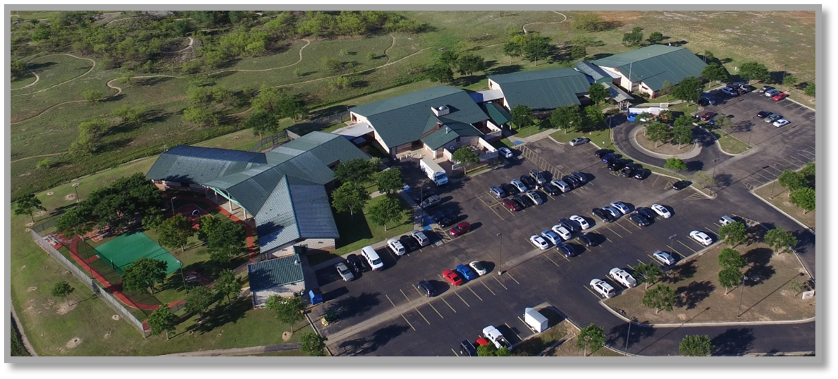 Aerial view of a hospital complex with a sports field and parking lot.
